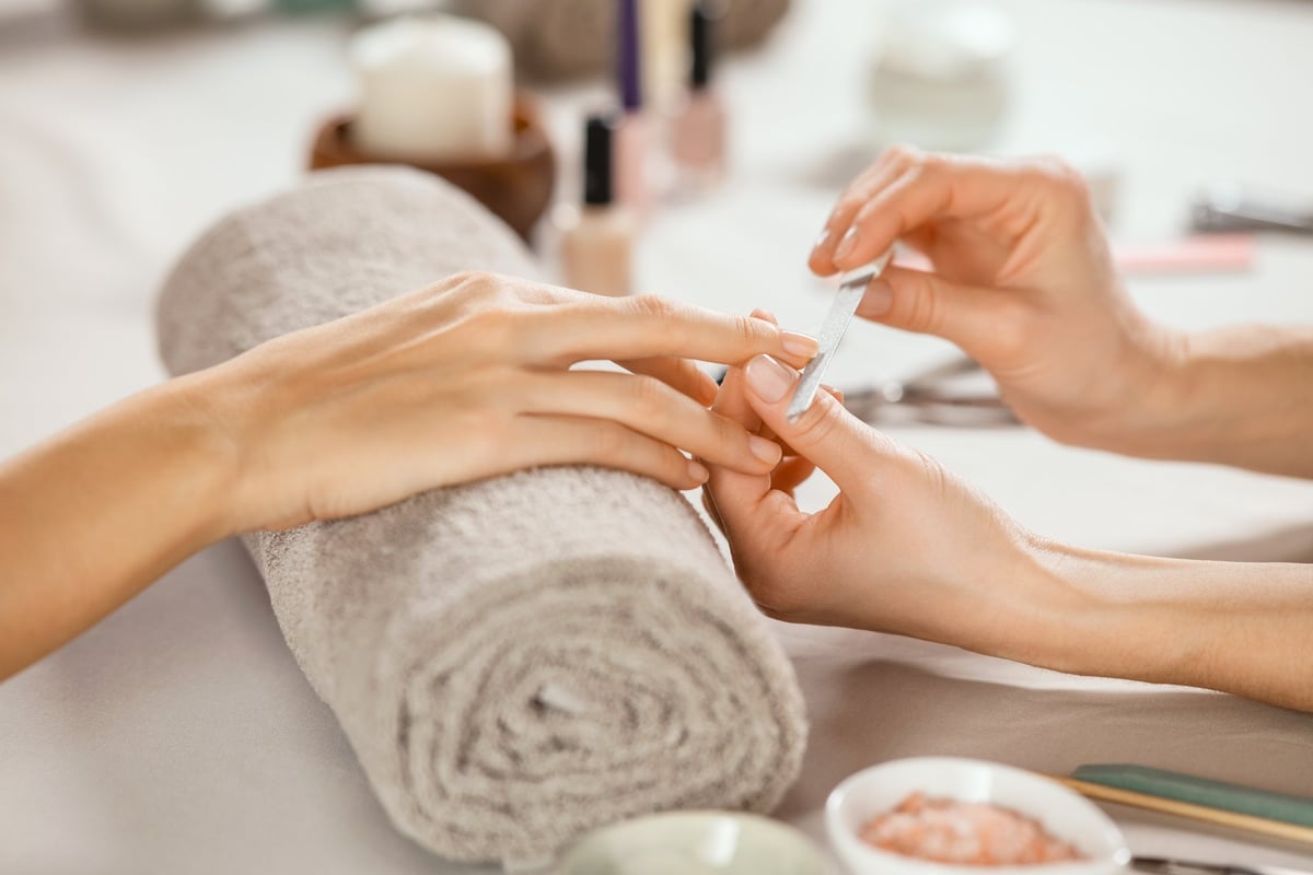 Close up shot of a woman in a nail salon receiving manicure by beautician with metal nail file